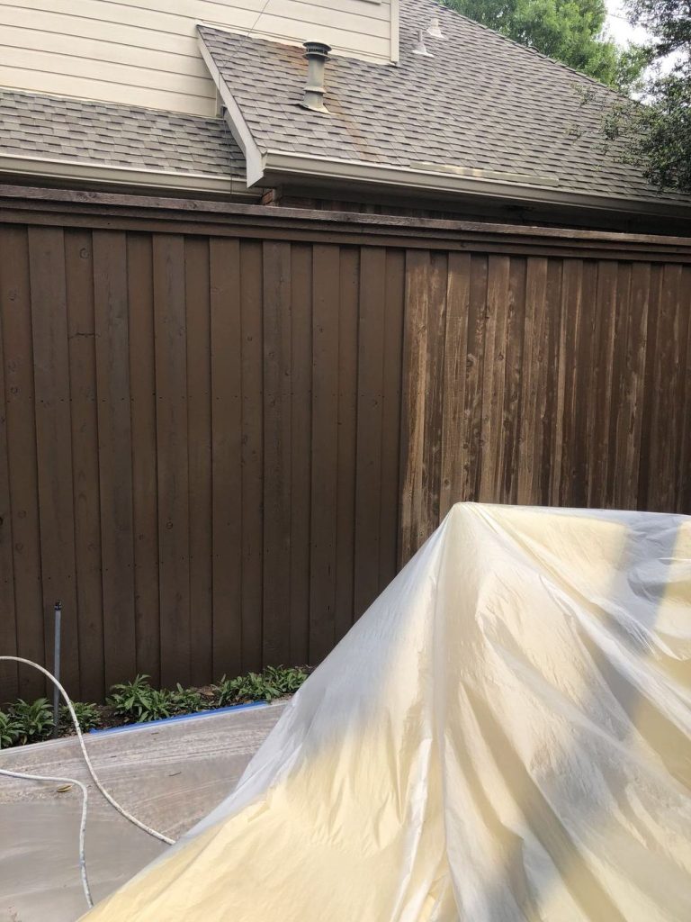 Fresh stain applied to a wood fence with landscaping protected