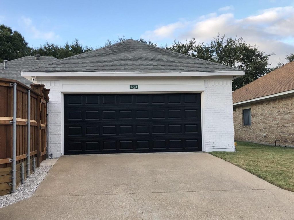 White painted brick garage with a black painted garage door