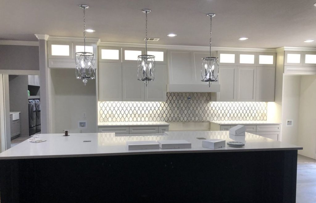 White painted kitchen cabinets with a black island and pendant lights