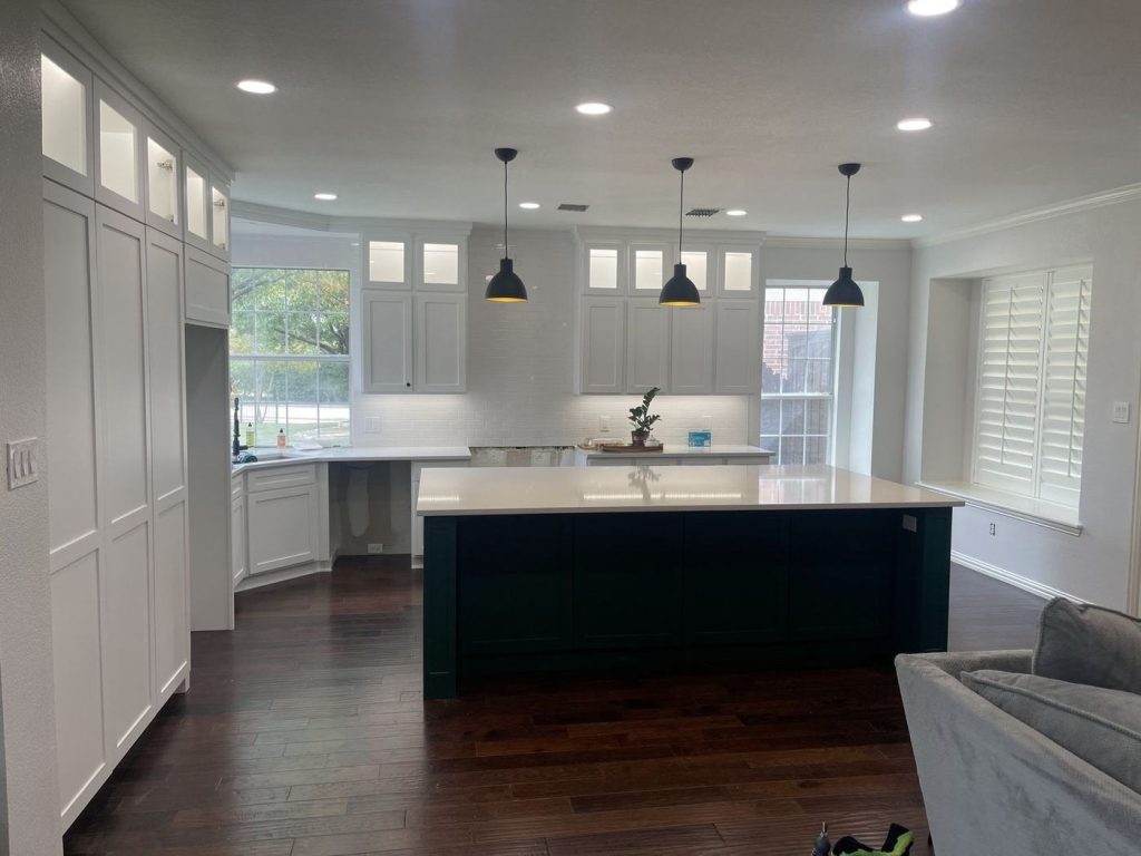 Wide view of a kitchen with white cabinets and a green island after painting
